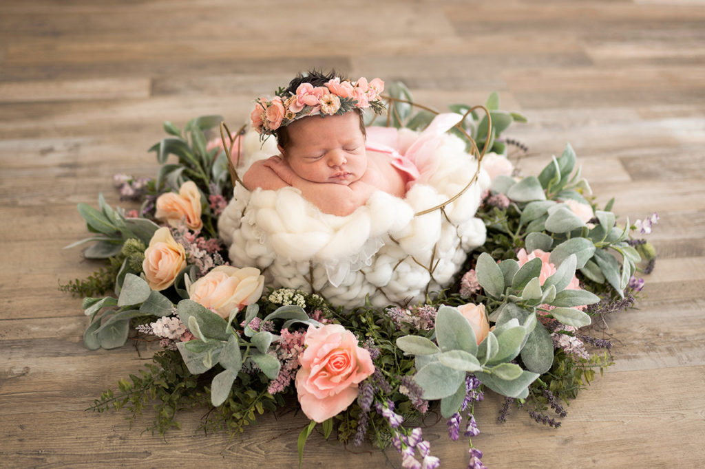 A newborn peacefully rests amidst a floral arrangement captured by Valentina Meza-Kohnenkampf, a Dallas-Fort Worth photographer.